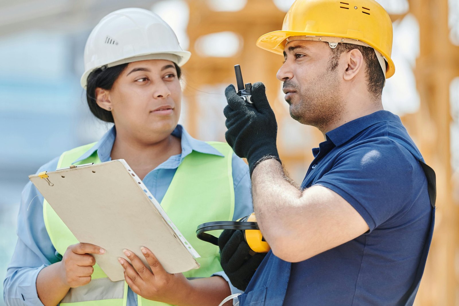 Home Two construction workers in safety gear discussing plans at a construction site.